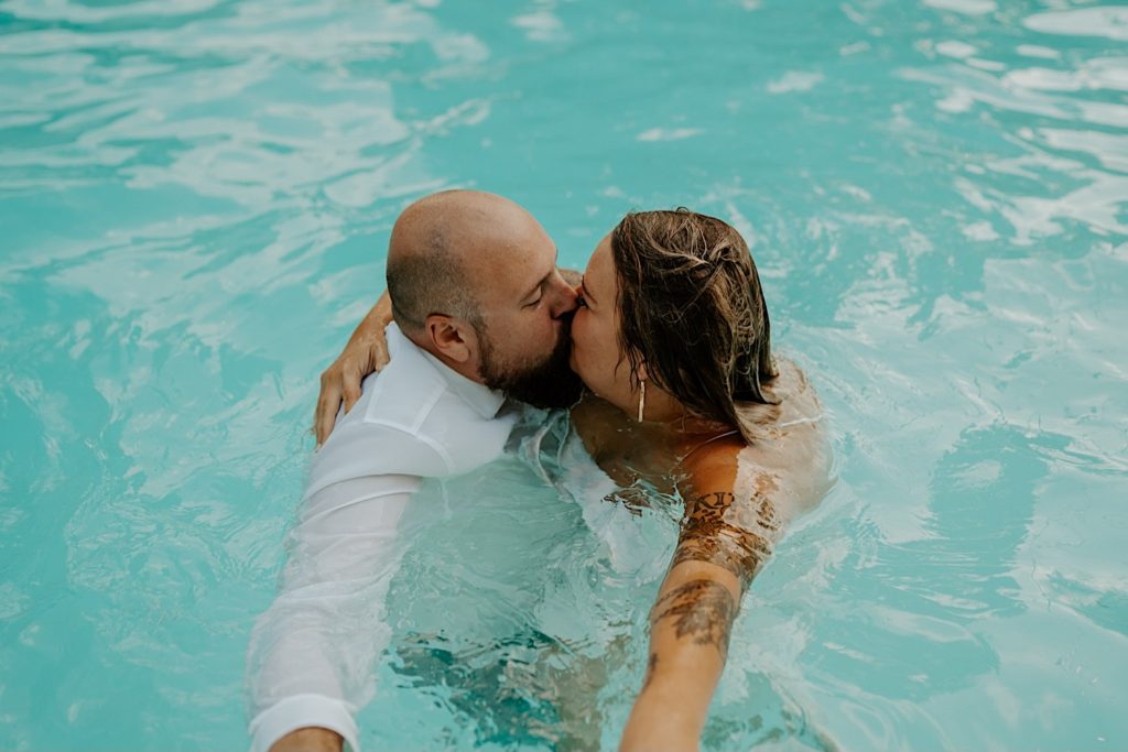 Bride and groom kiss while embracing in a swimming pool still wearing their wedding attire