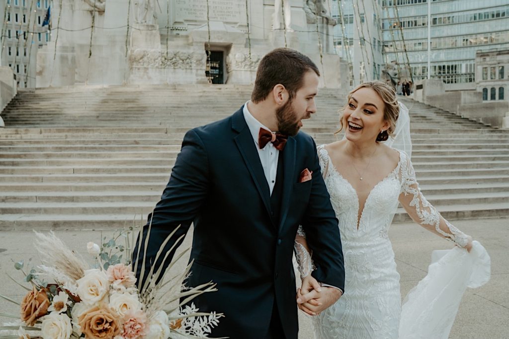 Bride and groom walking together and laughing in front of a stone staircase and building