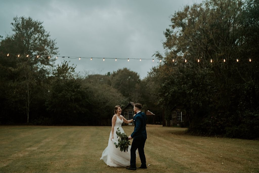 Bride and groom dancing in a field together under string lights