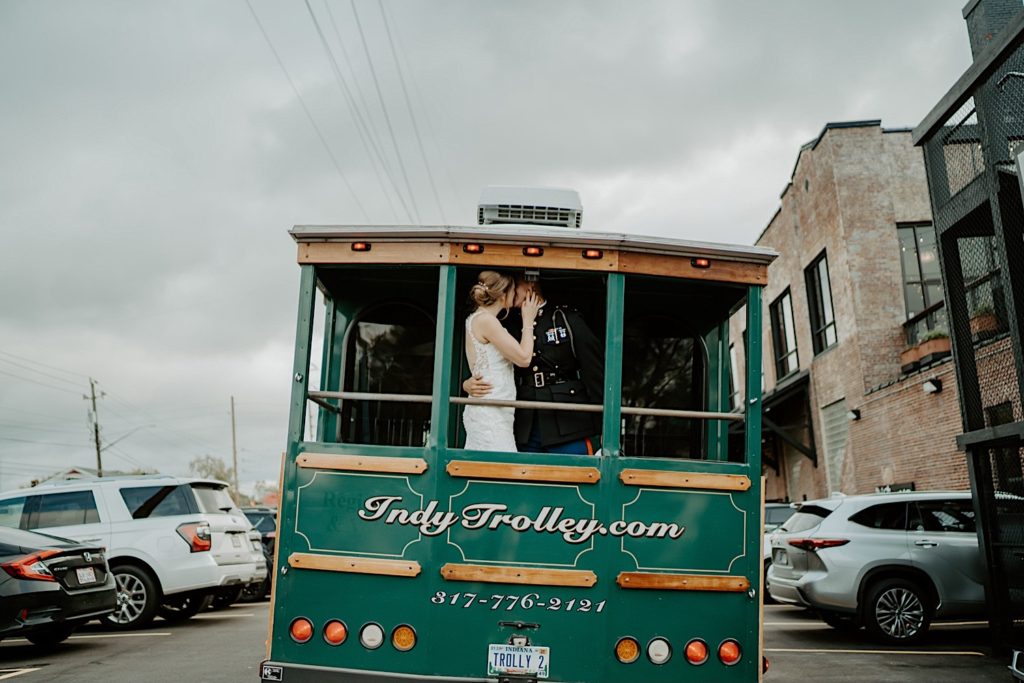 Bride and groom kiss while riding the Indy Trolley away from the camera