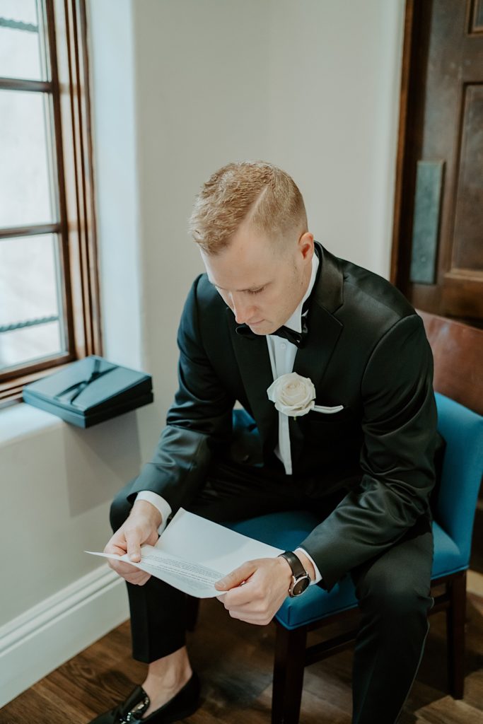 A groom dressed for his wedding sits and reads a letter from the bride before their wedding.