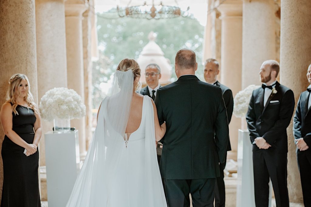 A bride walks down the aisle with her father away from the camera during her intimate Florida wedding ceremony.