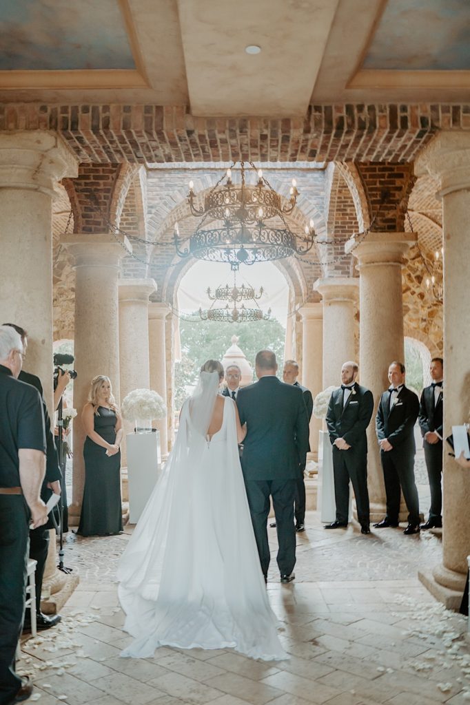 A bride walks down the aisle with her father away from the camera during her intimate Florida wedding ceremony.