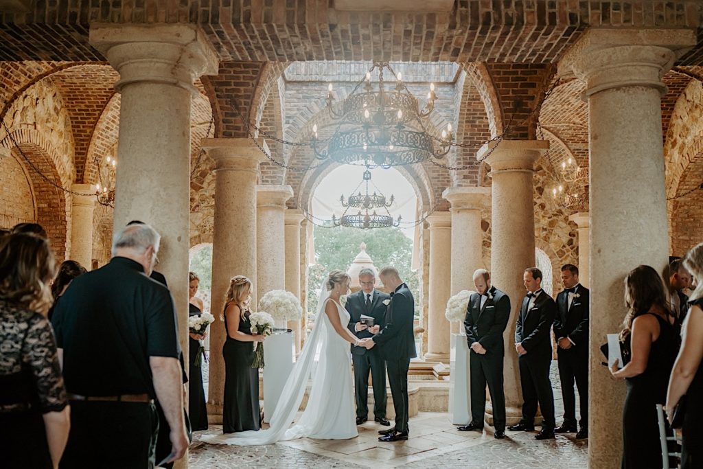 At an intimate wedding ceremony at Bella Collina in Florida a bride and groom both look down as they face each other holding hands with their officiant speaking behind them.