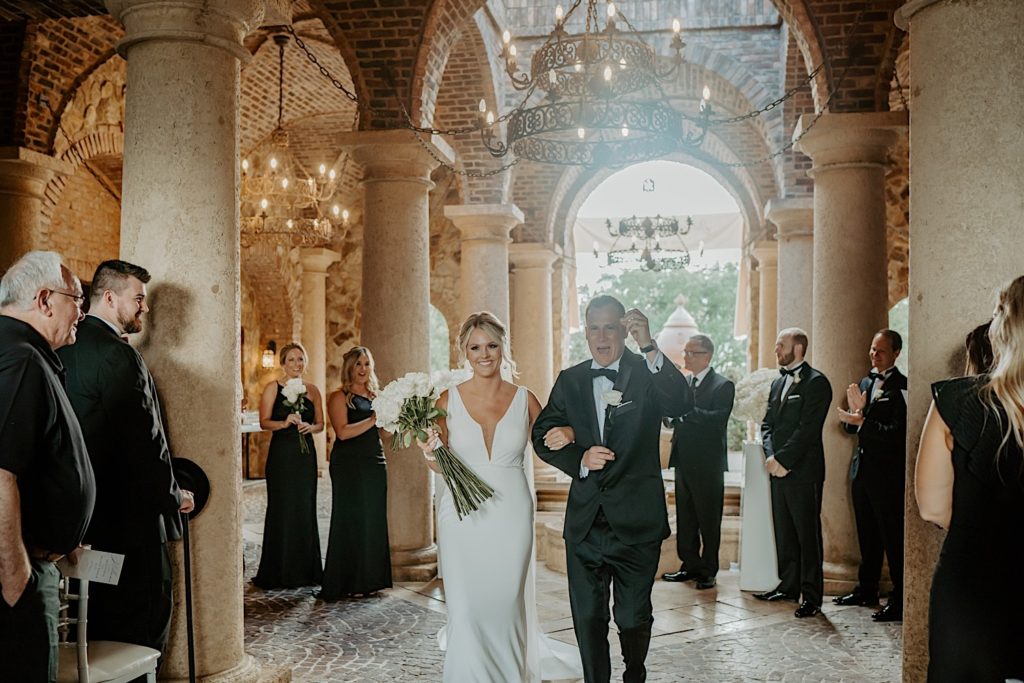 A bride and groom exit their intimate wedding ceremony at Bella Collina in Florida. Their arms are locked and the groom is cheering as the guests clap and celebrate around them.