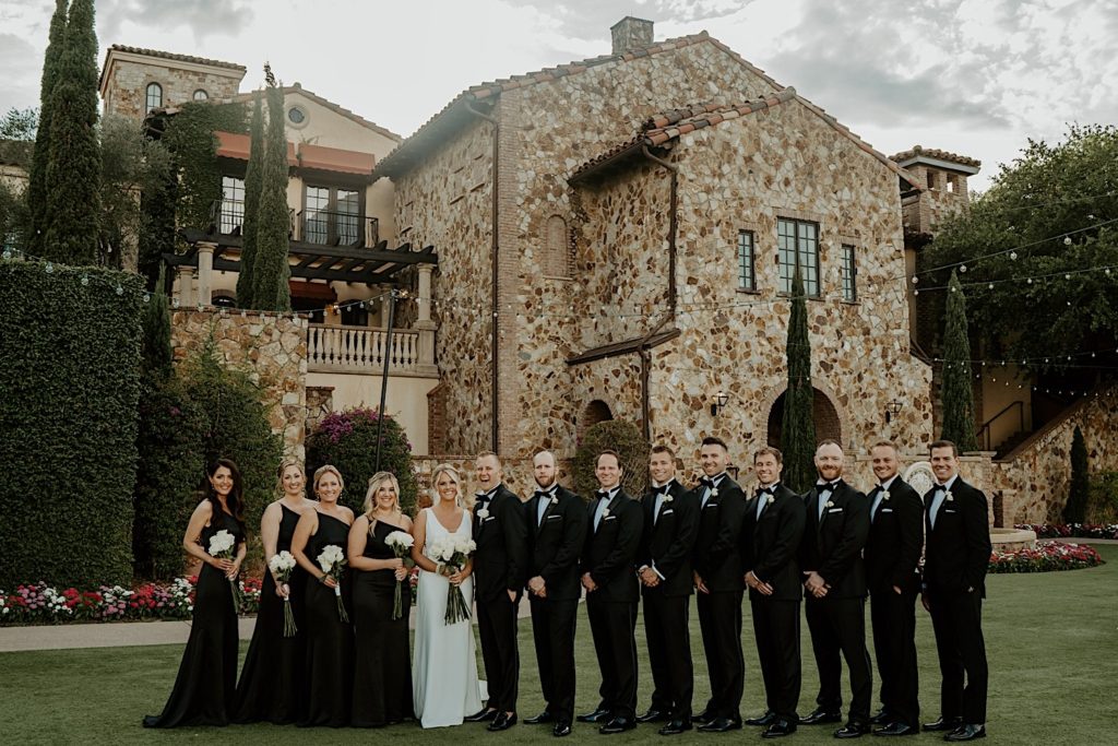 A bride and groom stand with their wedding parties on either side of them outside of their intimate wedding venue Bella Collina in Florida. Everyone is smiling at the camera.
