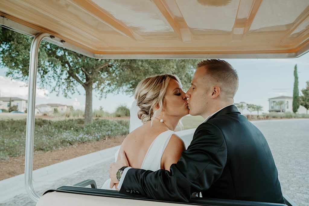 A bride and groom sit on a golf cart and kiss one another after their intimate wedding ceremony at Bella Collina in Florida