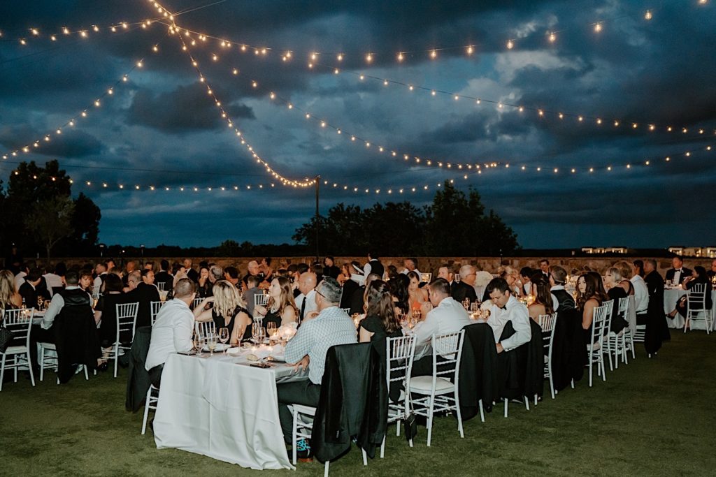 An outdoor intimate wedding reception at Bella Collina in Florida, guests are seated at tables with string lights and storm clouds above them.