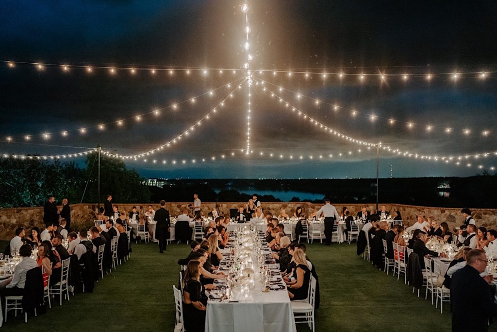 An outdoor intimate wedding reception at Bella Collina in Florida, guests are seated at tables with string lights and storm clouds above them.