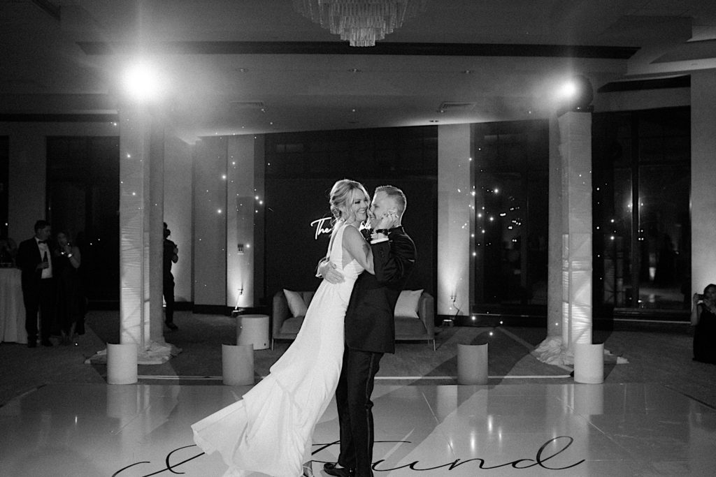Black and white photo of a bride being lifted into the air by the groom during their first dance of their intimate wedding reception.