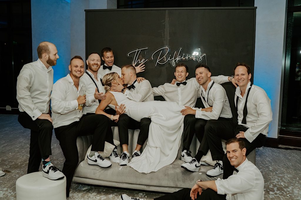 A bride kisses the groom with his groomsmen surrounding them