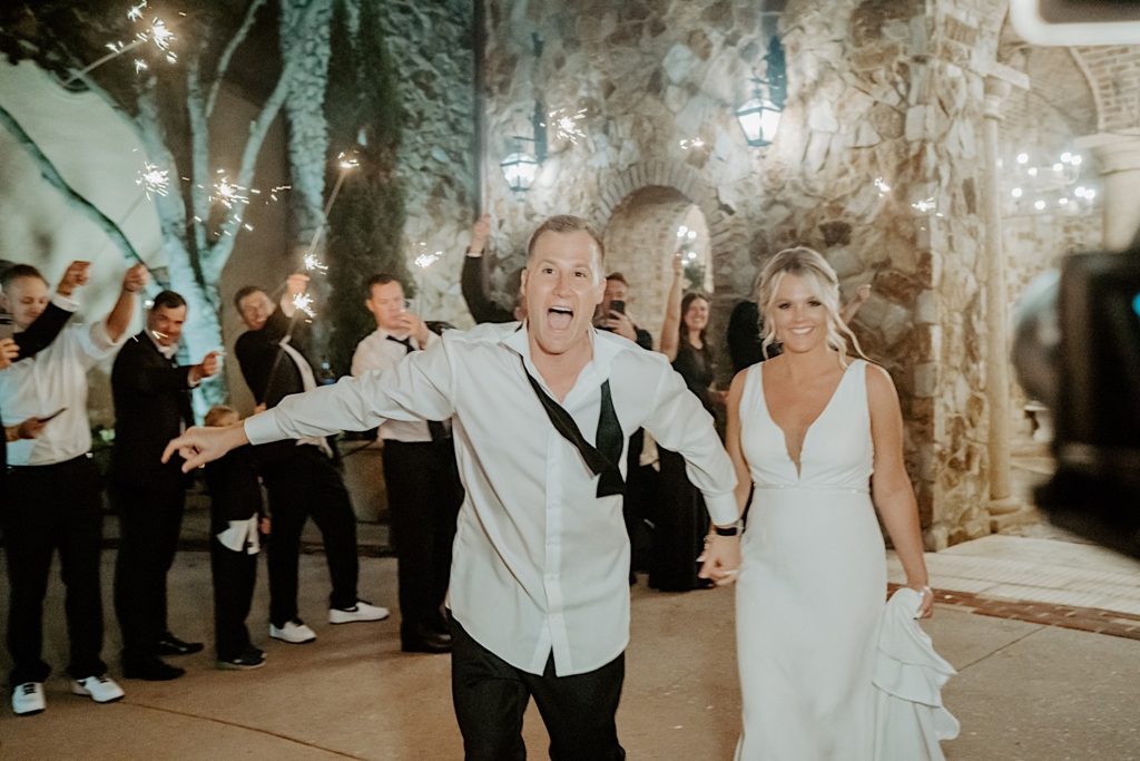 A bride and groom smile at the camera as they exit their intimate wedding reception at Bella Collina in Florida with their guests around them for a sparkler exit