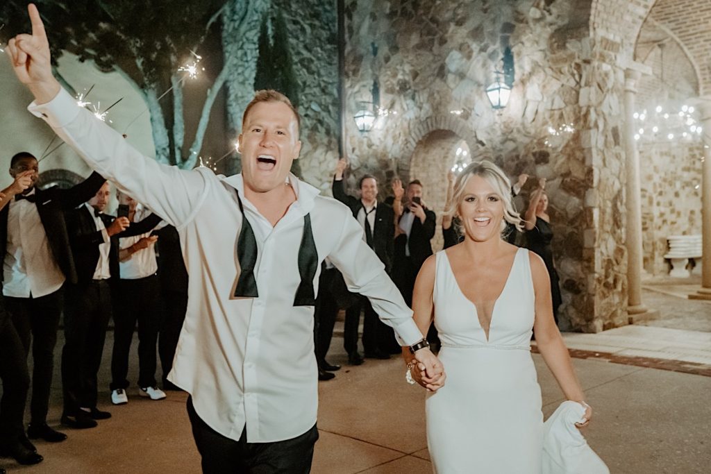 A bride and groom smile at the camera as they exit their intimate wedding reception at Bella Collina in Florida with their guests around them for a sparkler exit