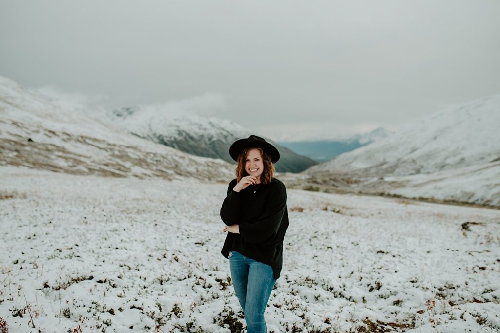 Photograph of Shelby Jane Photography, an Indiana elopement photographer, smiling at the camera with snow covered mountains in the background.
