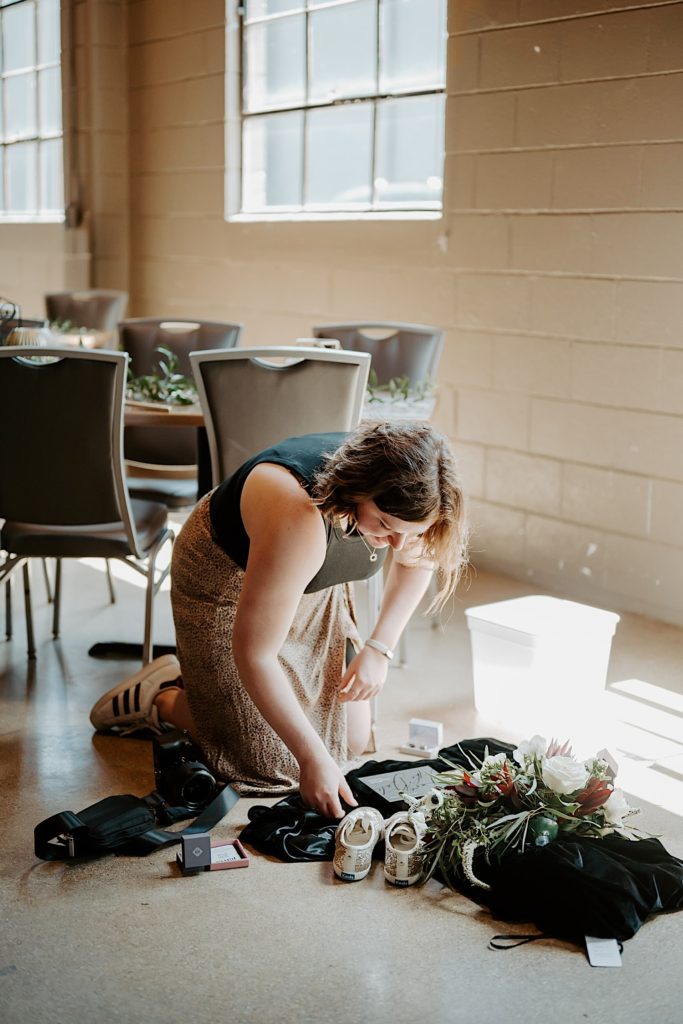 Photograph of Shelby Jane Photography, an Indiana elopement photographer, setting up a display of wedding details on the floor to photograph