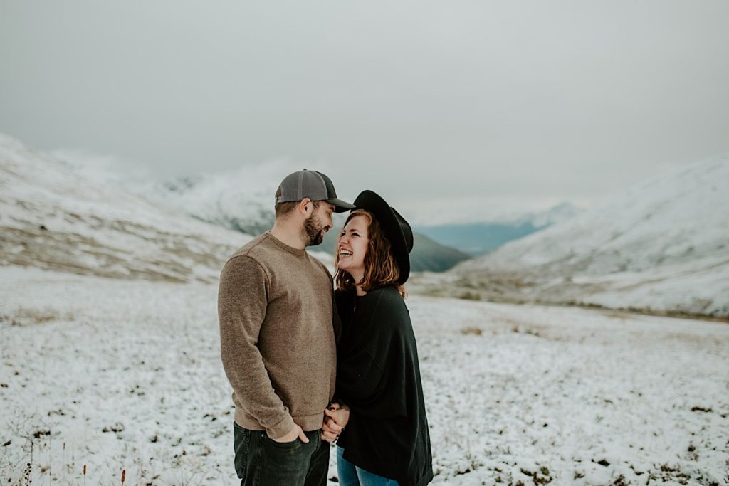 Photograph of Shelby Jane Photography, an Indiana elopement photographer, smiling at her partner with snow covered mountains behind them.