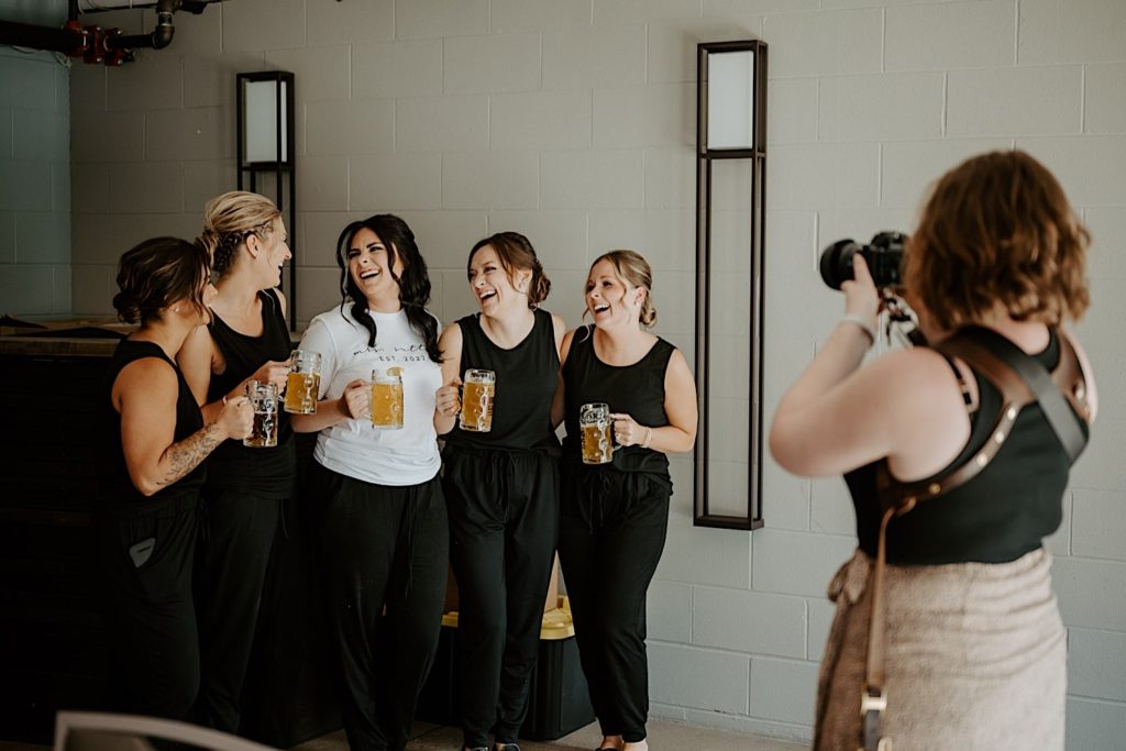 Photograph of Shelby Jane Photography, an Indiana elopement photographer, photographing a bride and her bridesmaids laughing with beer mugs in their hands