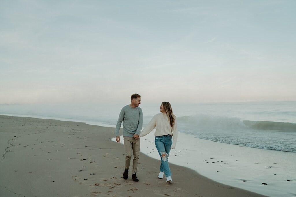 An engaged couple walks on the beach along the water at the Indiana Dunes.