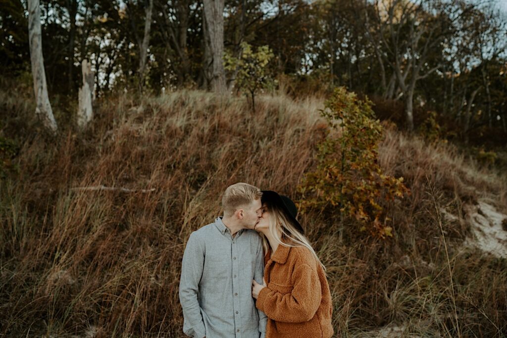 An engaged couple kisses during their engagement session at the Indiana Dunes State Park in the fall.