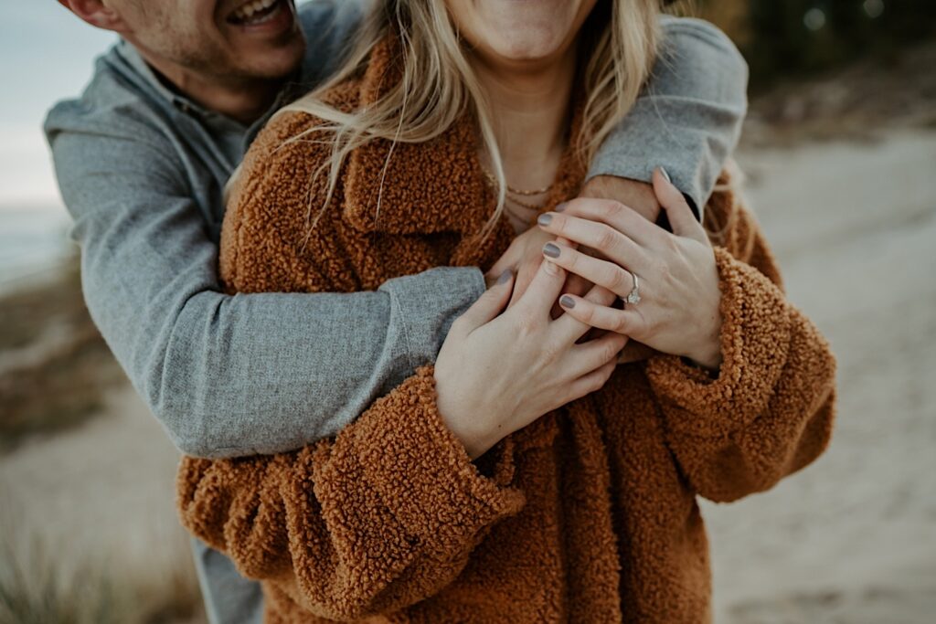 A close up image of an engaged couple hugging one another while showing off their fall outfits and her engagement ring.