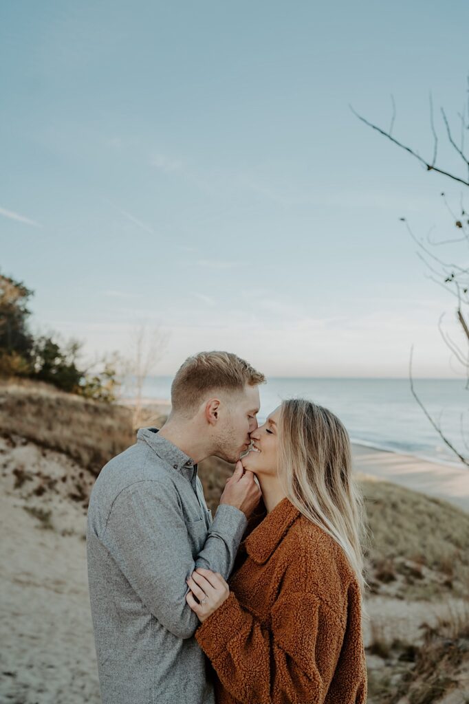 An engaged couple almost kisses while smiling on the beach at the Indiana Dunes