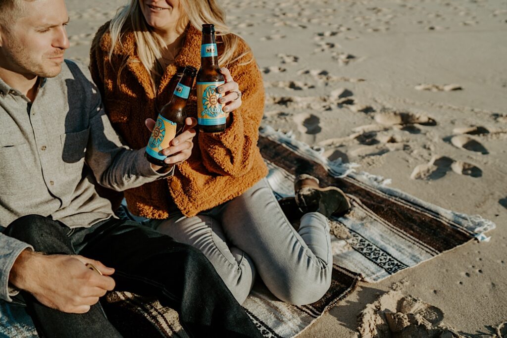 An engaged couple clinks their Oberon beer bottles showing off their engagement ring during their session.