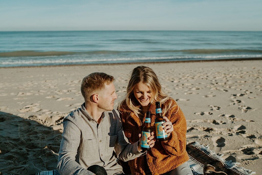 An engaged couple clinks their Oberon beer bottles showing off their engagement ring during their session.