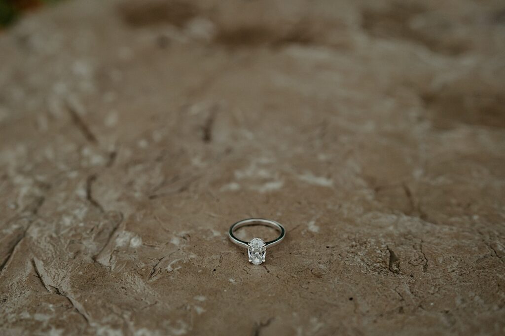 An oval cut engagement ring sitting on a wet stone