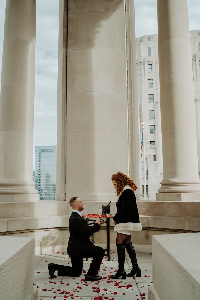 A man proposing to his fiancée at the Londonhouse Cupola surrounded by rose petals.