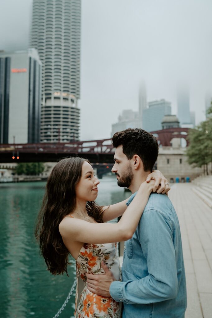 A fiancée holds his fiancé around her waist and she puts her arms around his shoulders while smiling at one another during their Chicago engagement session.