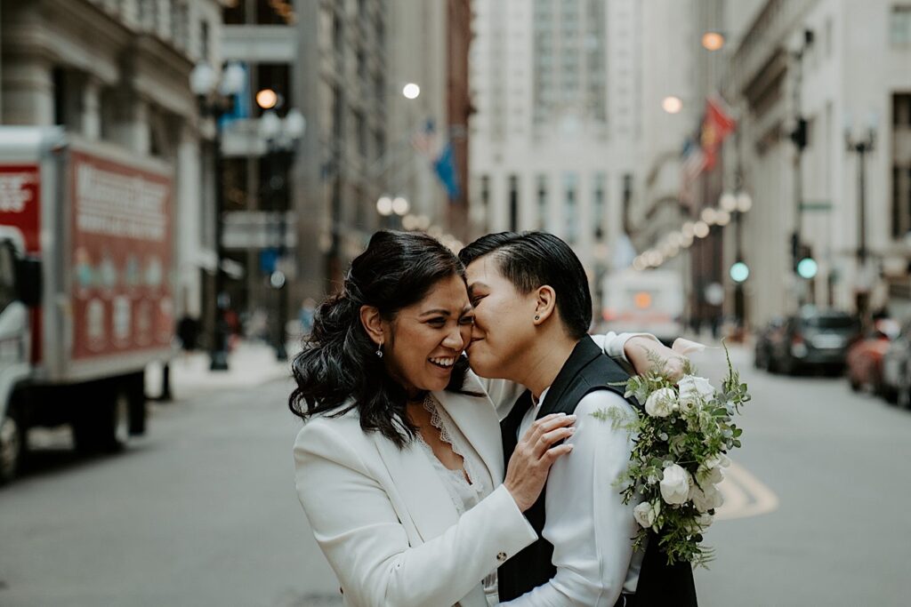 An lgbtq couple smiles while standing in the road in Chicago taking their wedding portraits.