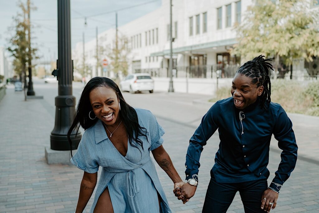 A couples smiles and laughs wearing blue outfits walking towards the camera in downtown Indianapolis