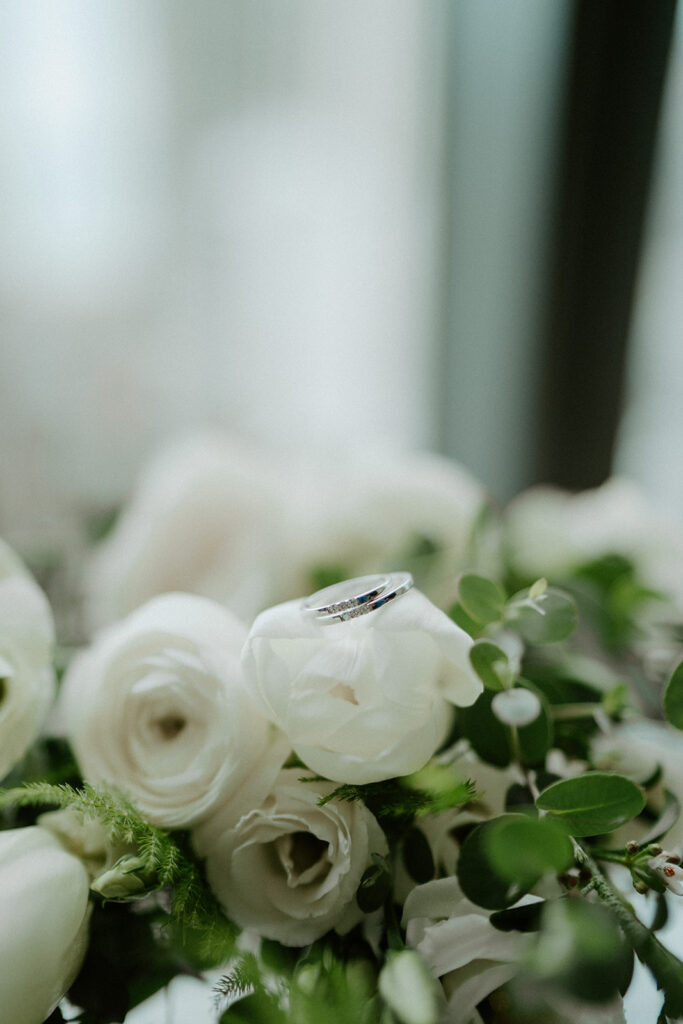 A pair of thin silver wedding bands, sitting on a white rose on the couples wedding morning.
