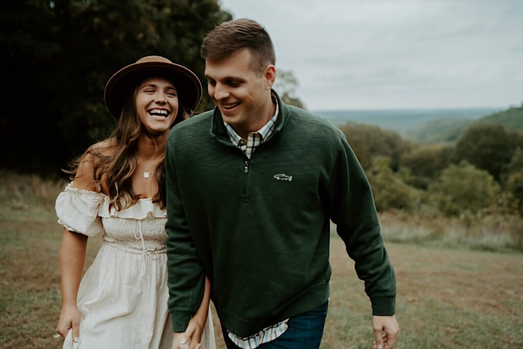 A fiancée smiles and laughs at her partner as they walk close to the camera.