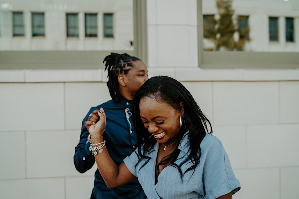 A couple both dressed in blue laughs candidly during their downtown Indianapolis engagement session.