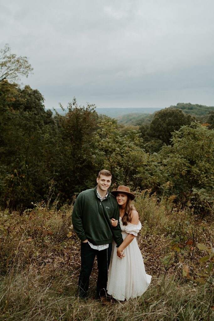 Fiancé's hold hands and smile at the camera while standing at a scenic location in Brown County State Park.