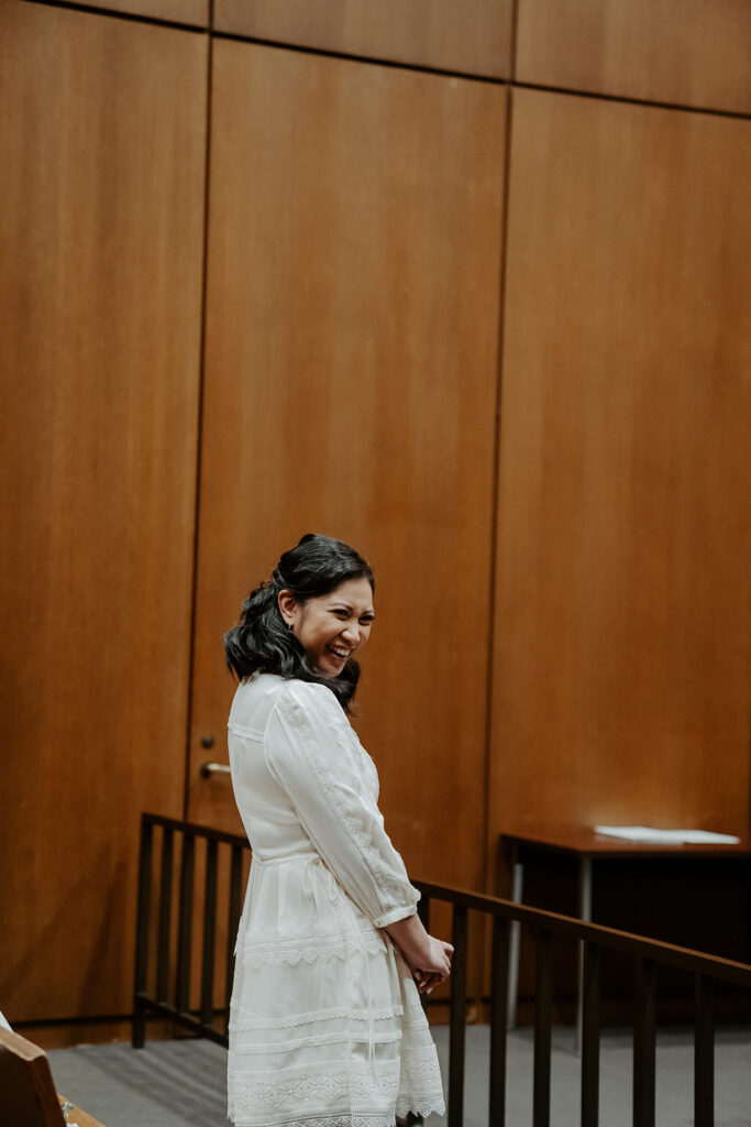 A bride smiles at her bride across the courthouse room as they begin their marriage ceremony.
