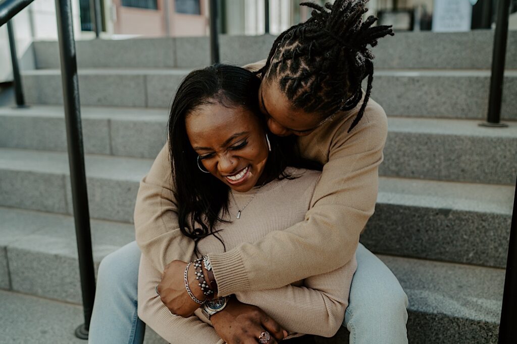 A couple hugs each other while sitting on marble steps together during their engagement session in Indianapolis.