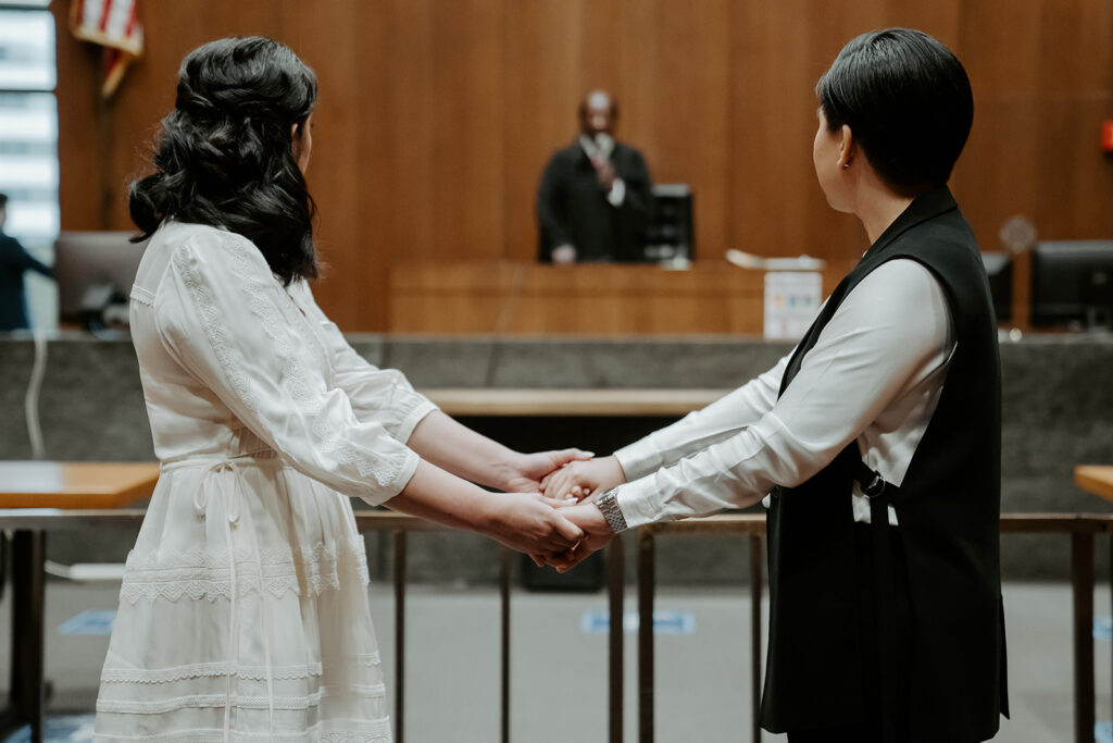 Two brides hold hands during their wedding ceremony at the Cook County Courthouse.
