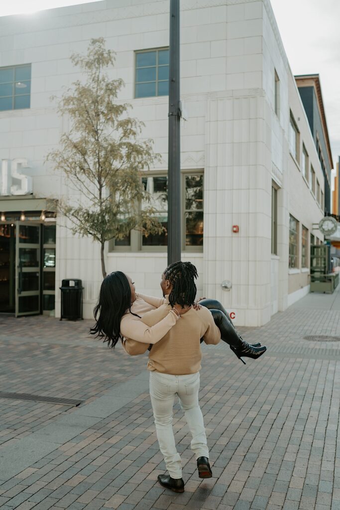 A fiancé carries his soon to be wife across the street during their engagement session.