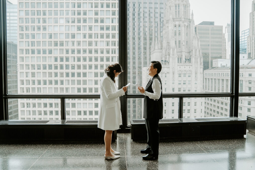 Brides stand together exchanging their vows in a Chicago skyscraper with the Tribune Tower in the background.