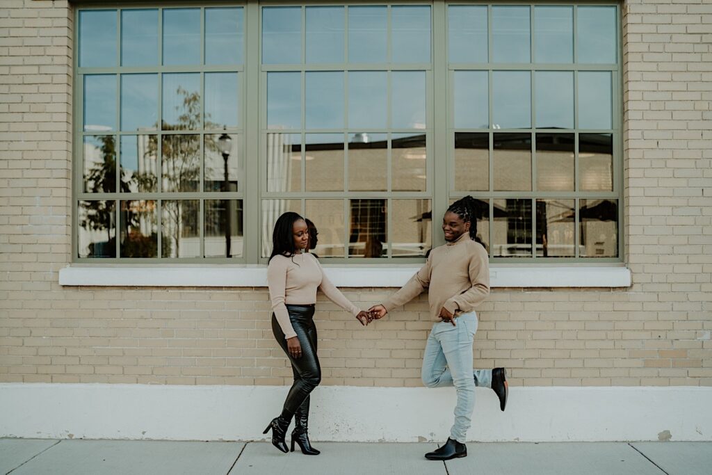 A couple stands holding hands during their engagement session in downtown Indy looking at one another.