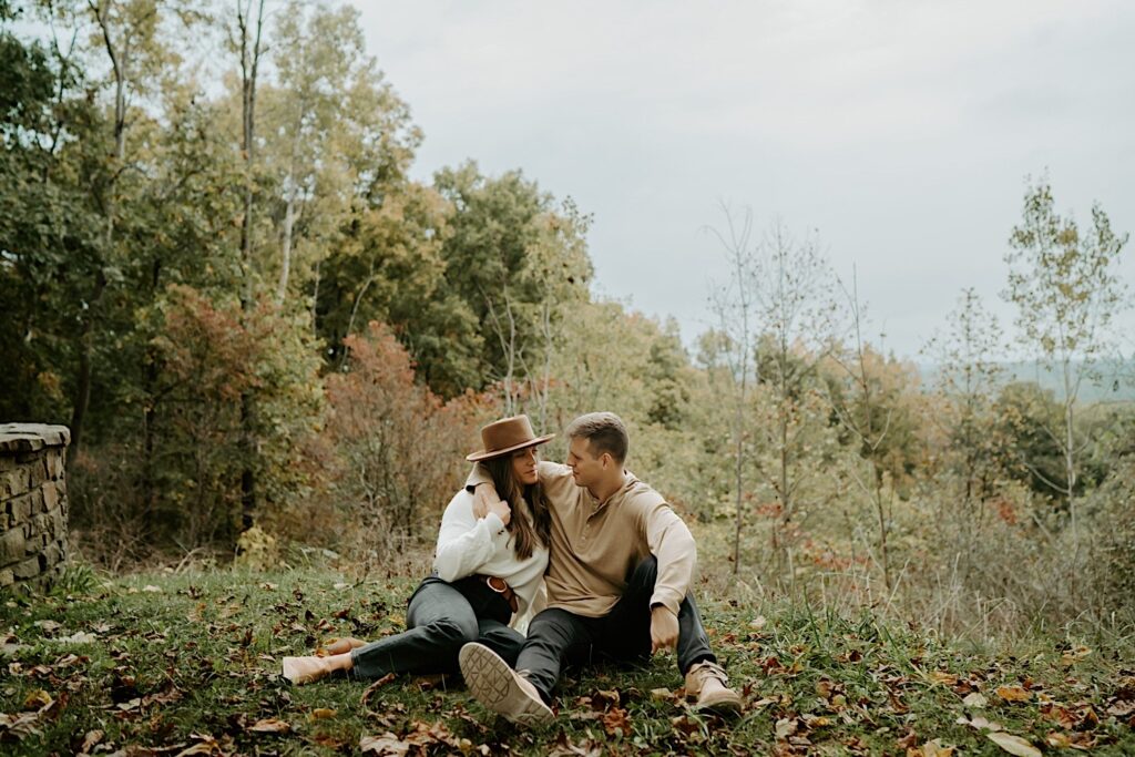 A couple sits together during their engagement session near an overlook at a forest preserve in Indiana