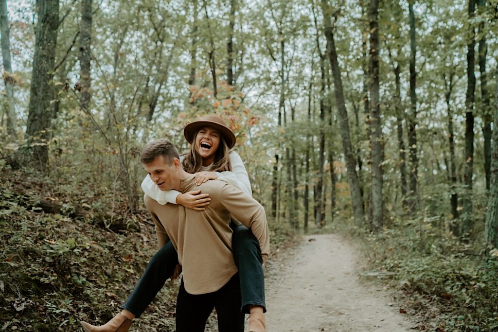 A fiancée rides on her fiancés back during thier forest engagement session in Indiana.