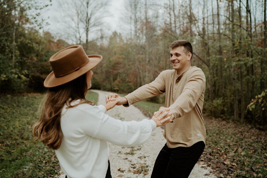 Fiancées in cute fall outfits during their engagement session in Indiana spin and hold hands