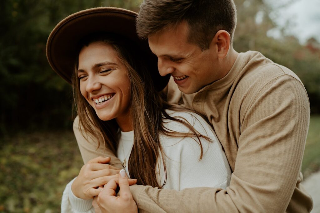 Fiancées hugging and laughing during their fall engagement session in a forest in Indiana