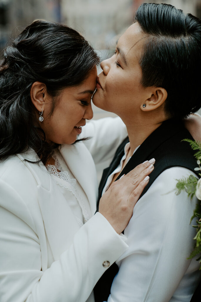 Newly weds stand in the middle of a street in Chicago sharing an intimate moment with one another.  One bride kisses her bride on the forehead.