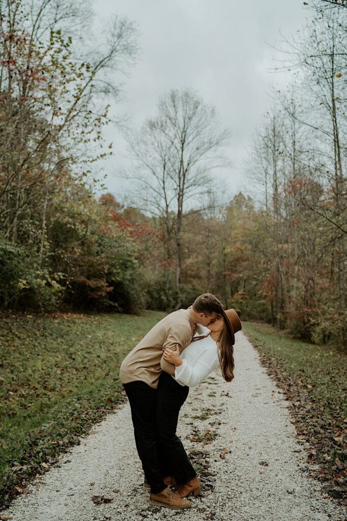 A couple hugs and kisses passionately on a gravel path during their engagement session at Brown County State Park