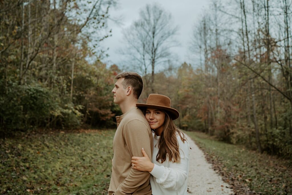Fiancées hold each other tight and look towards the camera in an Indiana forest during their engagement session.
