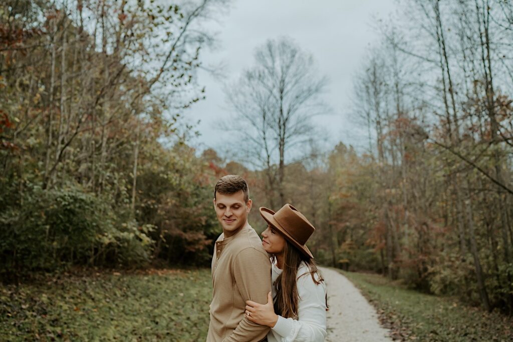 Fiancées hold each other tight and look towards eachother in an Indiana forest during their engagement session.